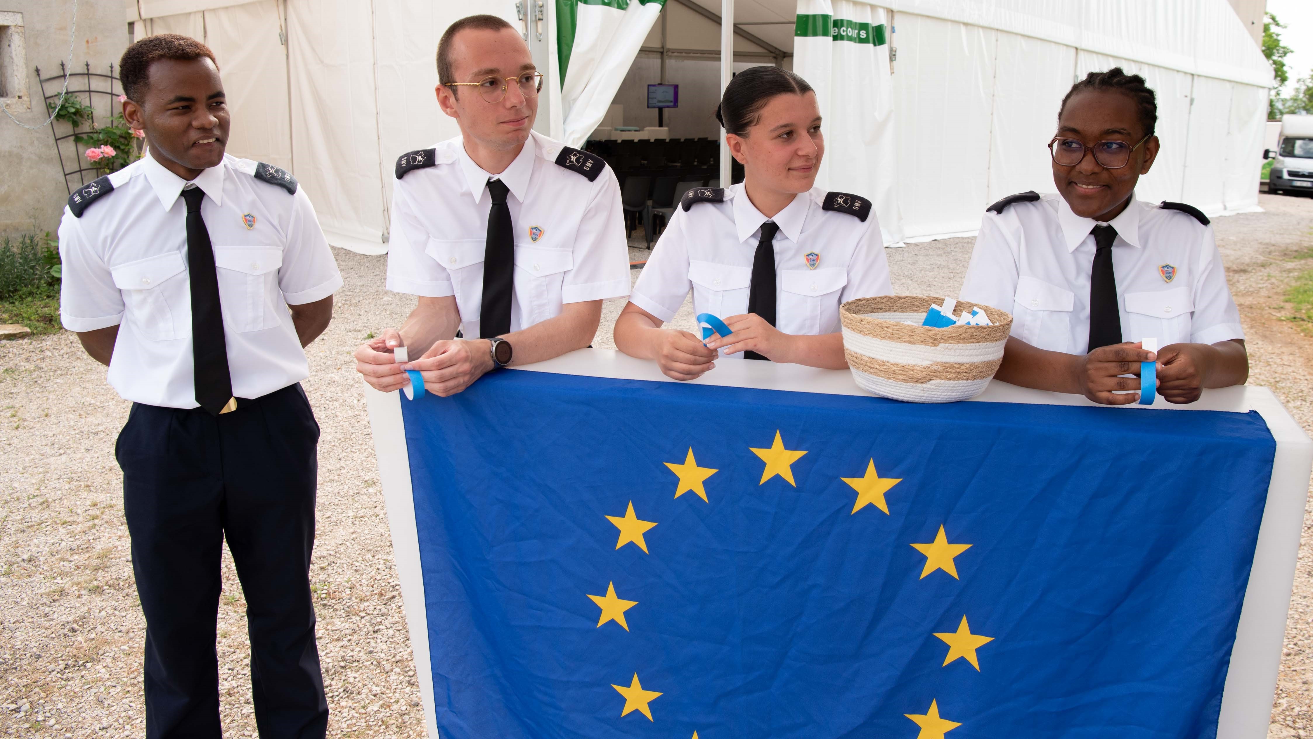 Four young participants of the voluntary military service stand at a high table with the European flag.