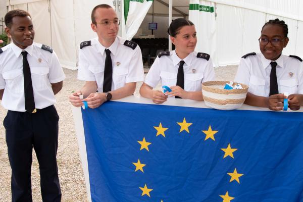 Four young participants of the voluntary military service stand at a high table with the European flag.